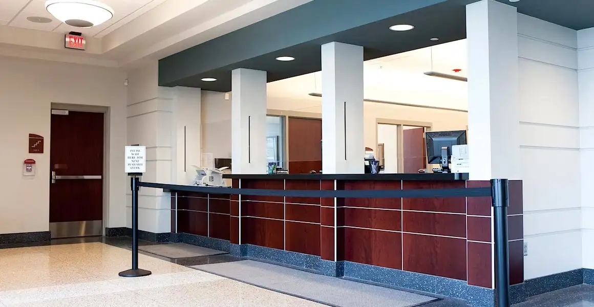 A spotless, freshly cleaned bank lobby in Riyadh showing polished wooden teller counters, a stanchion queue line, bright recessed lighting, and immaculate flooring.